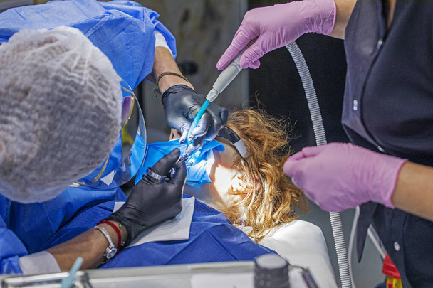 οδοντίατρος θεραπεία ένα άρρωστο δόντι σε έναν ασθενή μαζί με έναν βοηθό - Φωτογραφία, εικόνα