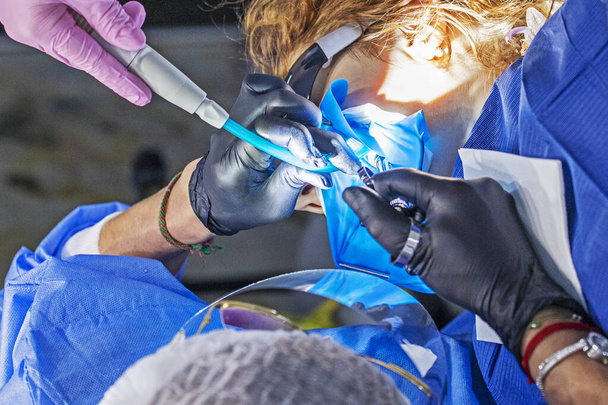 tandarts behandelen van een zieke tand aan een patiënt samen met een assistent - Foto, afbeelding