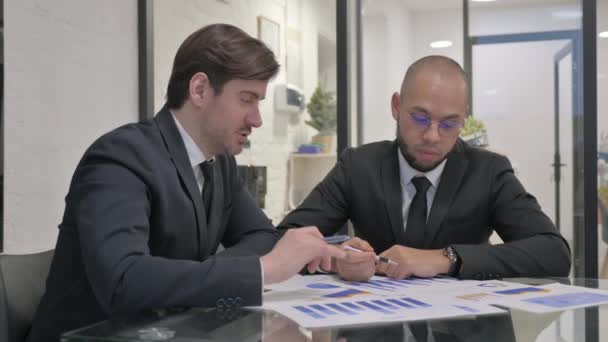 Молоді бізнесмени обговорюють документи в офісі - Кадри, відео