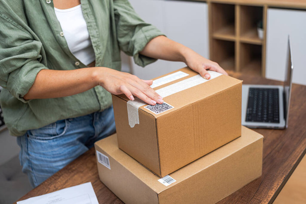 Naadloos verbonden: Womans handen brengen een QR code sticker aan op een pakket, die de essentie van online winkelen en e-commerce levering toont.  - Foto, afbeelding