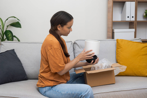 Decor Devotee: A shopaholic woman joyfully inspects her fresh home decor parcel, affirming contentment through e-commerce and swift online shopping delivery.  - Photo, Image