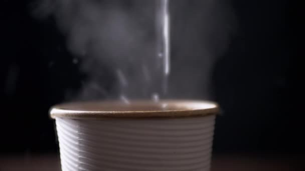 Preparando chá quente em uma xícara de papel em um fundo preto. Um fluxo de água fervente quente derrama em uma xícara de chá, vapor. Movimento lento, iluminação. Espaço para cópia. Bebe qualquer coisa. Vista lateral, isolada. Bebida de café. - Filmagem, Vídeo