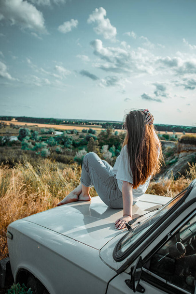 Деревенская девушка позирует на природе со своей старой машиной Лада на закате - Фото, изображение