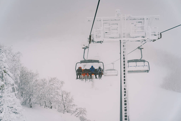 Sedačková lanovka s turisty v lyžařských kombinézách vyjede na mlhavou horu. Kvalitní fotografie - Fotografie, Obrázek