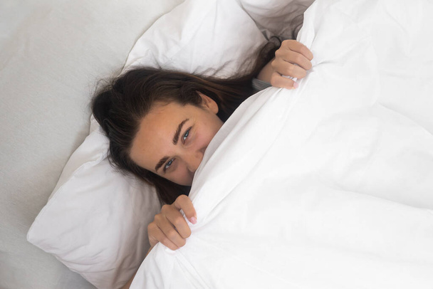 輝くスタート:陽気な女性は,ベッドで快適な朝に明らかに白い毛布で彼女の顔を覆う.  - 写真・画像