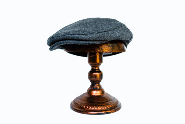 Detail einer schuppigen Mütze oder Schiebermütze oder aus Tweed-Fischgrat, montiert auf einem Bronzekopf auf weißem Hintergrund. Katalogfoto eines klassischen dunkelgrauen Hut auf einer eleganten Schaufensterpuppe aus Bronze - Foto, Bild