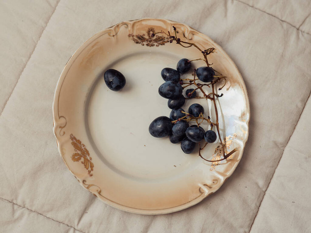 Minimal still life: Vertical close up shot of black grapes on a vintage beige plate. - Photo, Image