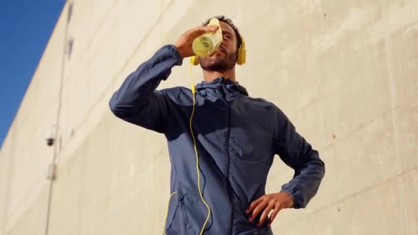 hombre atlético con auriculares sonriendo agua potable mientras hace ejercicio. - Metraje, vídeo