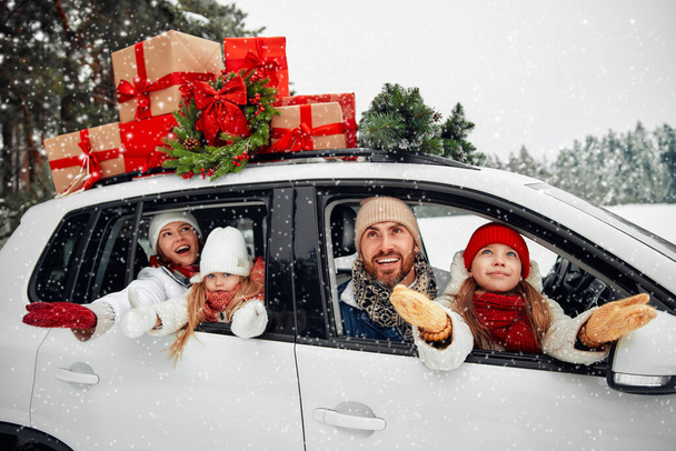 Veselé Vánoce a šťastný nový rok. Šťastná rodina s dětmi sedící v autě naloženém krabicemi dárků a vánočním stromečkem na pozadí lesa ve sněžném počasí. - Fotografie, Obrázek