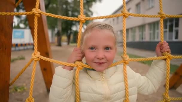 Маленька мила європейська дівчинка, що грає на ігровому майданчику, показує язик усміхненої радості весела школярка дитяче місто за межами вуличного дитинства спортивні розваги задоволення дозвілля дитячі пригоди учня - Кадри, відео