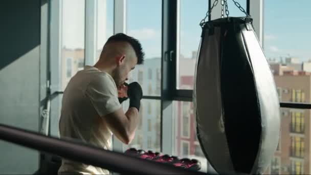 Unavený sportovec trénink box s boxovací pytel v moderní fitness tělocvičně otírání pot vyčerpaný kavkazský sport muž sportovec bojovník boxer cvičení se rány profesionální box cvičení silná motivace - Záběry, video