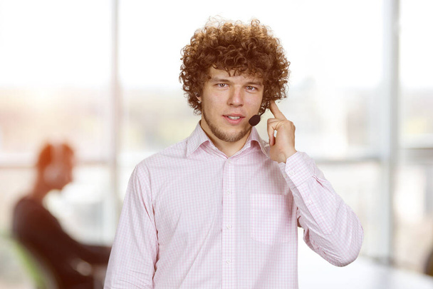 Young serious successful man in curly hair talking in microphone. Office interior in the background. - Photo, Image