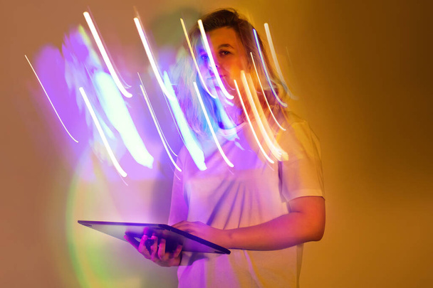 Stylowa praca z tabletem cyfrowym w odcieniach neonu. Stylowa młoda kobieta w białej koszuli z cyfrową tabletką w kolorowym neonie inspirowane oświetleniemt. - Zdjęcie, obraz