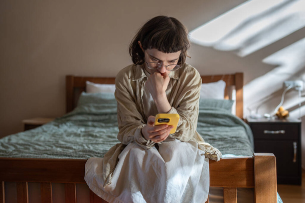 Nervous, stressed teen girl in glasses reading messages in smartphone feeling bad, humiliated. Depressed frustrated woman receive negative message in social media from haters. Cyberbullying, stalking. - Photo, Image