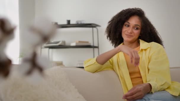 Beautiful young girl African American ethnic woman smiling happy dreamy calm healthy female sit on couch sofa comfortable rest relax dreaming with closed eyes inspired dreams harmony relaxing at home - Footage, Video