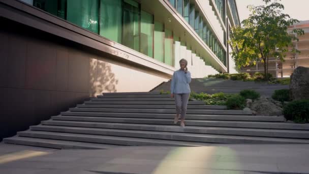 Glückliche kaukasische lächelnde alte Frau reif grauhaarige Geschäftsfrau Unternehmer sprechen Handy Lächeln zu Fuß die Treppe hinunter ins Freie Geschäftsfrau mittleren Alters beantworten Smartphone-Anruf in der Stadt außerhalb - Filmmaterial, Video