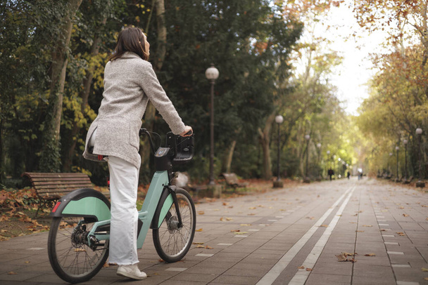 Mujer lista para montar en bicicleta en el parque de la ciudad, vista trasera, espacio de copia. Propósitos, objetivos, nuevo concepto de carretera. Foto de alta calidad - Foto, Imagen