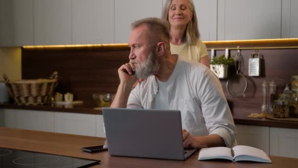 Senior middelbare man gepensioneerde zakenman op afstand werkende computer studeren online op laptop denken beslissing in de keuken volwassen glimlachen vrouw vrouw helpen zorg ondersteuning man thuis Kaukasische familie liefde - Video
