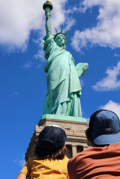 Syn i tata patrzący na Statuę Wolności (Liberty Oświecający Świat), niesamowitą miedzianą posąg zbudowaną przez Gustave 'a Eiffla w 1886 roku w Nowym Jorku. - Zdjęcie, obraz