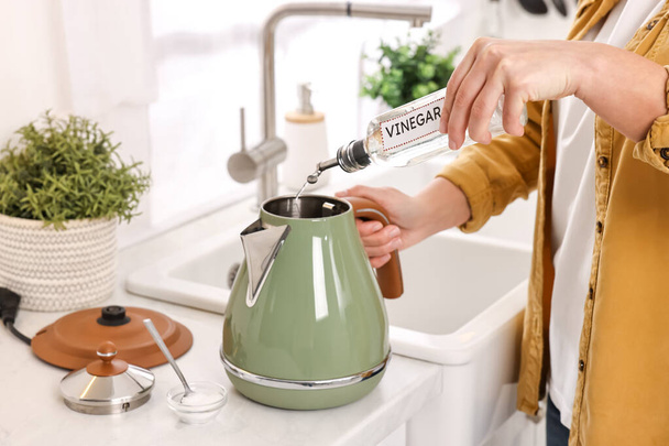 Woman pouring vinegar from bottle into electric kettle in kitchen, closeup - Foto, imagen