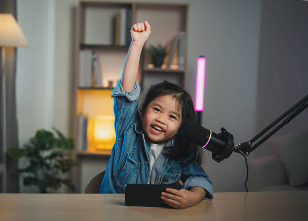 Asiatique influenceur jeune fille sourire gai à l'aide de téléphone mobile jeu en direct streaming salutations vidéoconférence avec ordinateur portable et le port d'un casque. Enfants streaming casting jeu concept en ligne. - Photo, image