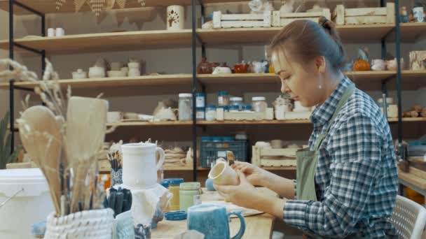 Dívka maluje ručně vyrobený hrnec s barvami v dílně - Záběry, video