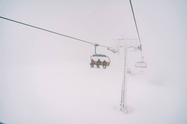 Лижники на чотиримісному кріслі їздять по горі через туман. Високоякісна фотографія - Фото, зображення