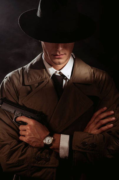 Silhouette of a male detective in a coat and hat with a gun in his hands. A book drama noir portrait in the style of detectives of the 1950s - Zdjęcie, obraz