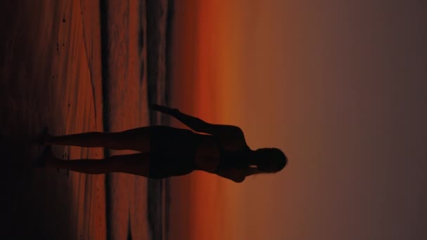 Video verticale. Affascinante donna sportiva sul mare Effettua con grazia un esercizio. Routine fitness. Atleta Stretching le mani sul tramonto. Allenamento fisico. Concetto Sport e Persone - Filmati, video