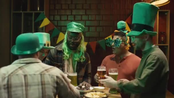 Střední záběry mužského barmana servírujícího silné pivo ženě, která slaví národní den irských svatých Patricků s různými přáteli popíjejícími zelené pivo v baru - Záběry, video