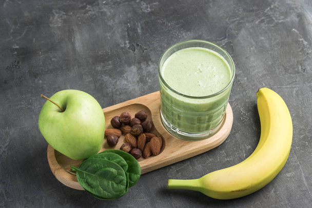 Zöld méregtelenítő turmix egy pohárban, kevert vegetáriánus ital spenótlevélből, alma, banángyümölcs és diófélék sötét alapon, egészséges étkezési koncepció. - Fotó, kép
