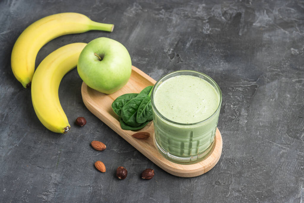 Zelený detoxikační koktejl ve sklenici, míchaný vegetariánský nápoj z listů špenátu, jablko, banánové ovoce a ořechy na tmavém pozadí, zdravý stravovací koncept. - Fotografie, Obrázek