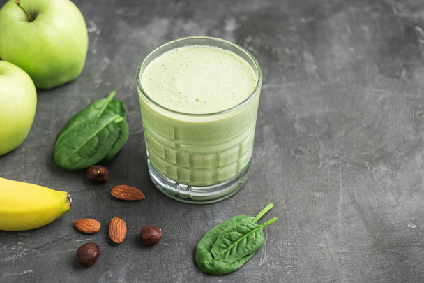Πράσινο smoothie detox σε ένα ποτήρι, αναμεμειγμένο χορτοφαγικό ποτό από φύλλα σπανακιού, μήλο, φρούτα μπανάνας και ξηρούς καρπούς σε σκούρο φόντο, έννοια υγιεινής διατροφής. - Φωτογραφία, εικόνα