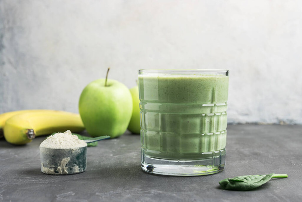 Zelený detoxikační koktejl ve sklenici, odměrná lžička s proteinovým práškem, míchaný vegetariánský nápoj z listů špenátu, jablečné a banánové ovoce, zdravá výživa. - Fotografie, Obrázek