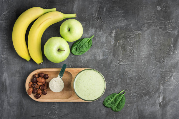 Zöld méregtelenítő turmix egy pohárban, mérőkanál fehérjeporral, kevert vegetáriánus ital spenótlevélből, alma és banángyümölcs sötét alapon, egészséges étkezési koncepció, felülnézet. - Fotó, kép