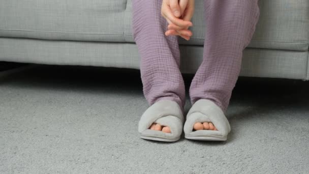 Mujer en pijama y zapatillas sentada en sofá en contemplación. - Metraje, vídeo