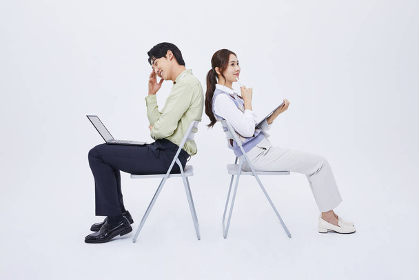 A man and a woman sitting back to back and playing a tablet with a laptop - 写真・画像