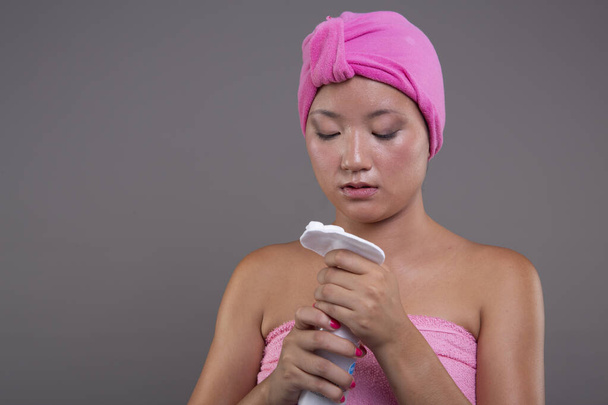Post-douche huidverzorging ritueel van een jonge Chinese vrouw, verpakt in handdoeken - Foto, afbeelding