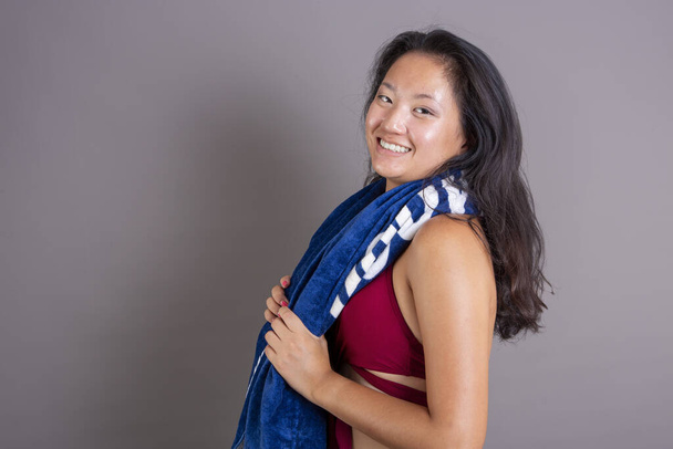 Una donna asiatica radiante con un asciugamano blu dopo l'allenamento - Foto, immagini
