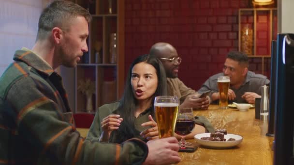 Lato medio scatto di Biracial donna parlando con fidanzato caucasico al bar con birra in serata - Filmati, video