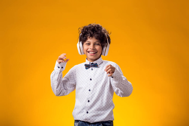 Portrait of child boy with headphone listening to music and dancing over yellow background. Leisure and lifestyle concept - Photo, Image