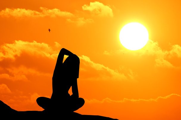 Silhouette einer Frau, die bei Sonnenuntergang am Meer Yoga praktiziert. - Foto, Bild