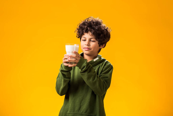 黄色の背景にミルクのグラスを持っている笑顔の子供の少年の肖像画. 健康食品コンセプト - 写真・画像