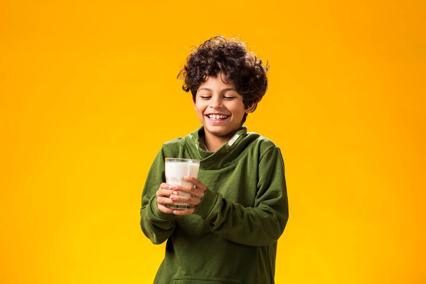 Портрет улыбающегося мальчика, держащего стакан молока на желтом фоне. Концепция здорового питания - Фото, изображение