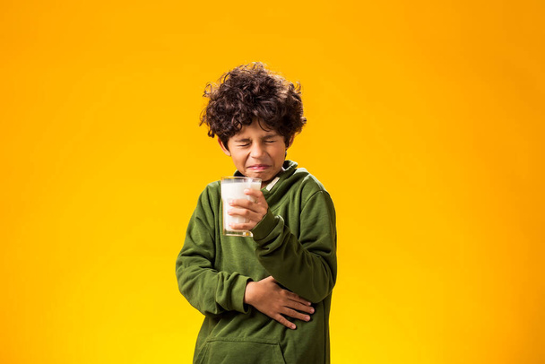 Intolerancia a la lactosa. Lácteos intolerante infeliz niño sosteniendo vaso de leche y sintiendo dolor abdominal sobre fondo amarillo.  - Foto, Imagen