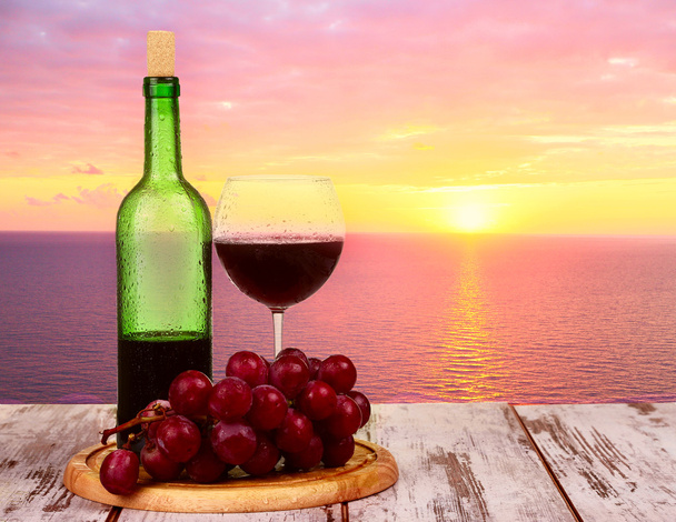 Bottiglia di vino con bicchieri di vino al tramonto sullo sfondo del mare
 - Foto, immagini