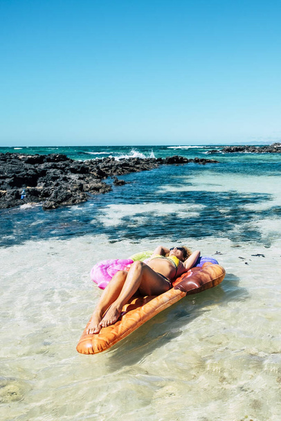 Hermosa playa y el agua tropical del océano con la mujer bonita se acuesta en un lilo inflable colorido del colchón que relaja y que goza de la naturaleza del mar y de la playa en vacaciones del verano - Foto, Imagen