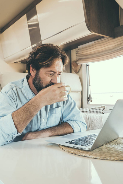 man use computer inside camper van during travel vacation or van life lifestyle. Modern man and woman work together on laptop in alternative office motor home. Digital nomad and smart free working - Foto, immagini