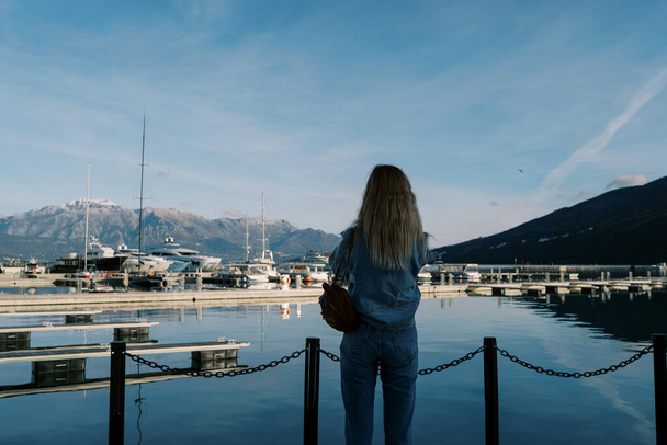 Woman stands on a pier by the sea and looks at the moored yachts. Back view. High quality photo - Photo, Image