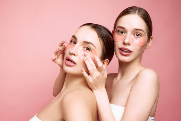 Glowing together. Unveiling natural beauty and hydration. Portrait of two young attractive girls applying under-eye moisturized patches. Concept of beauty treatments, morning routine, anti-aging, spa. - Photo, Image